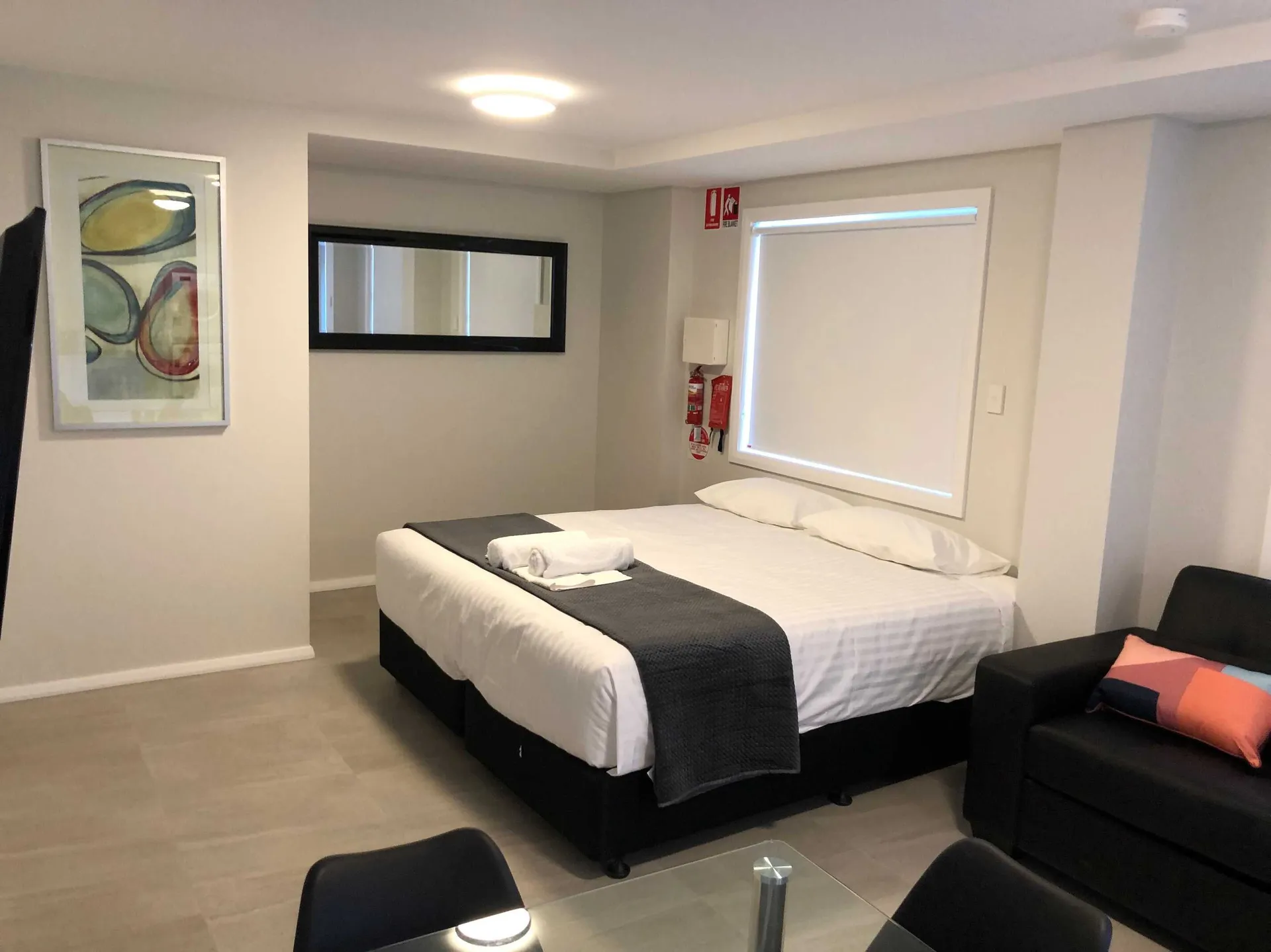 Studio apartment interior with queen bed, framed art, sofa with coral cushion and dining nook